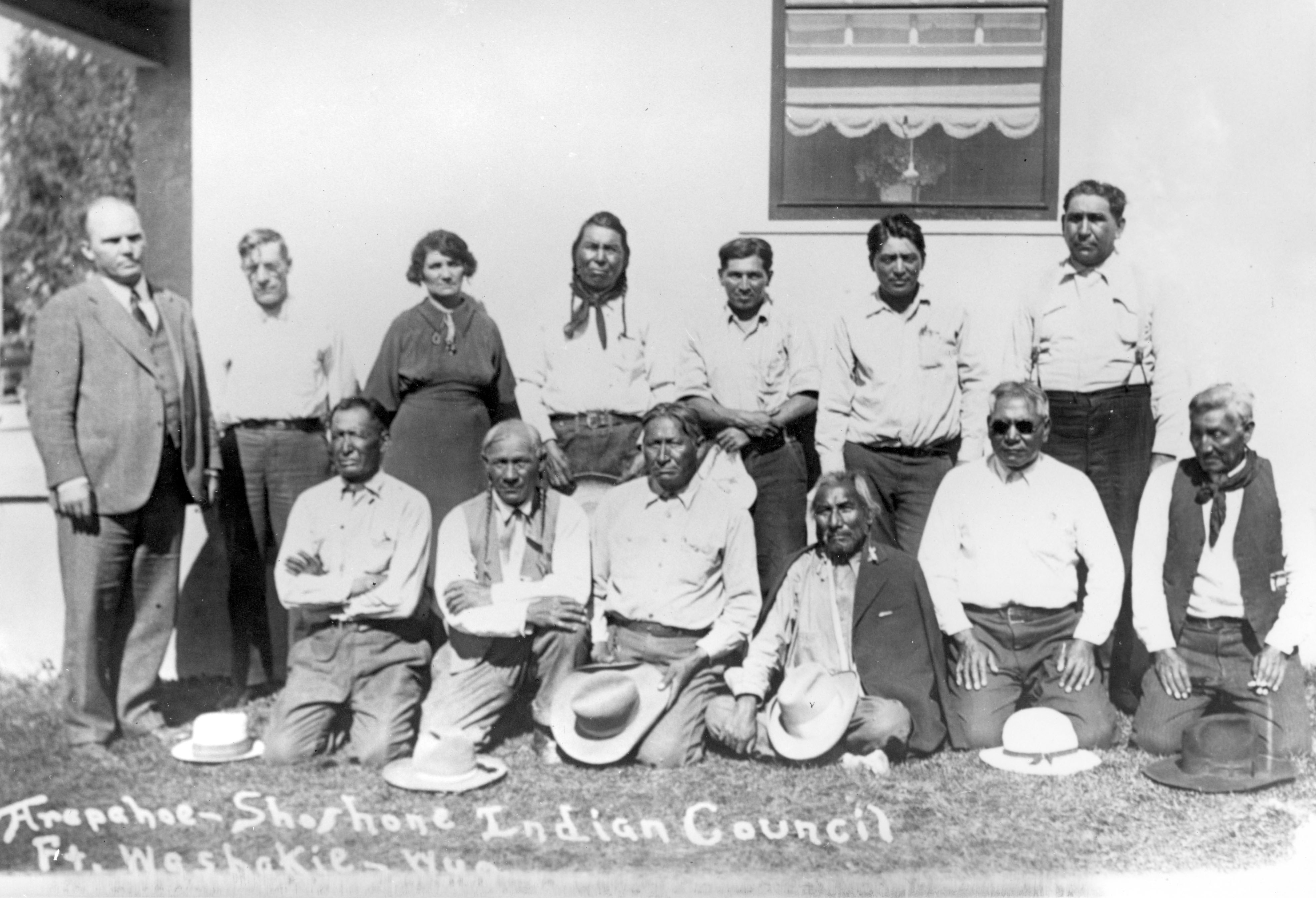 Two rows of people, the front row kneeling and the back row standing, with one woman standing in the back row.  The photograph is labeled Ft. Washakie Wyo.